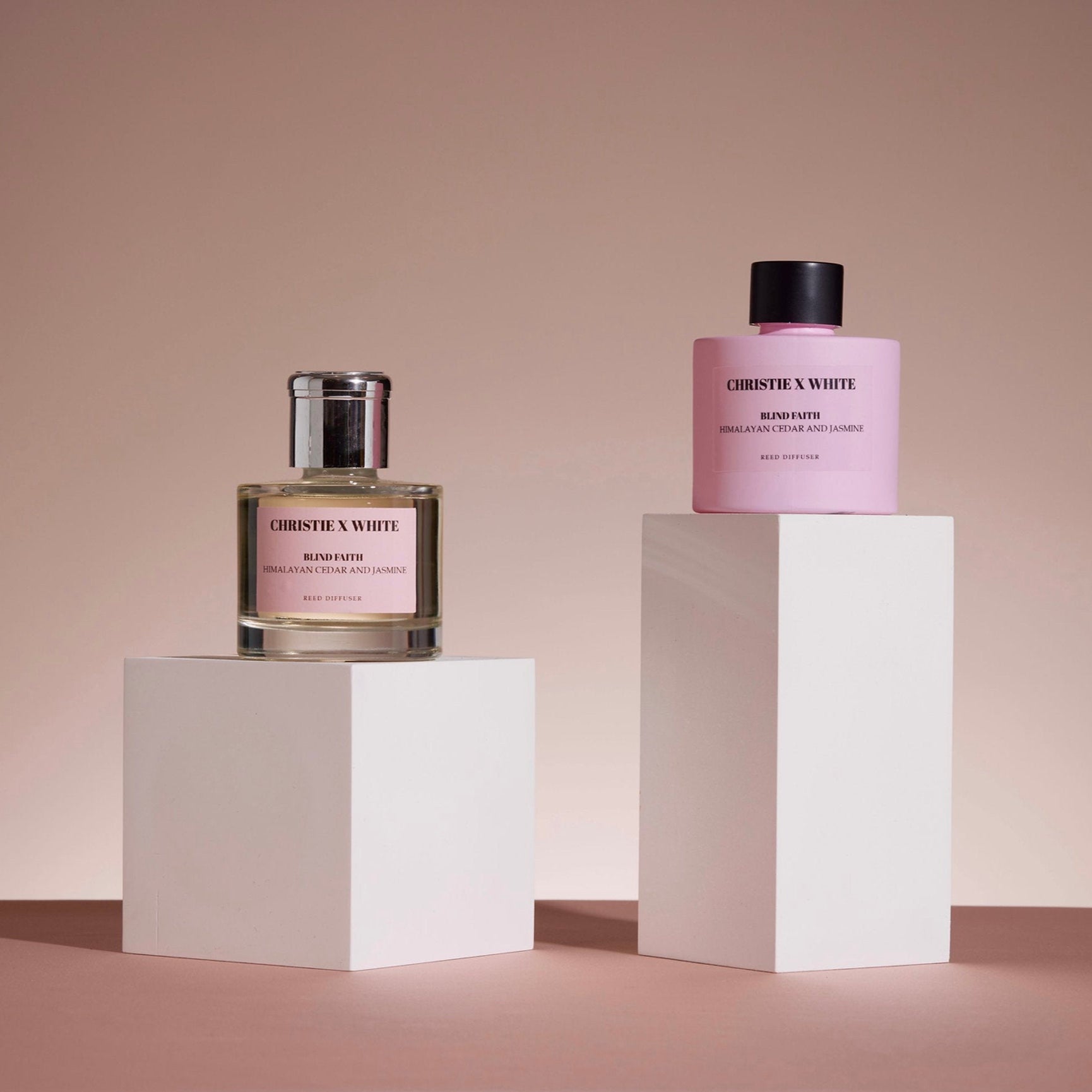 Two perfume bottles on white pedestals against a beige background