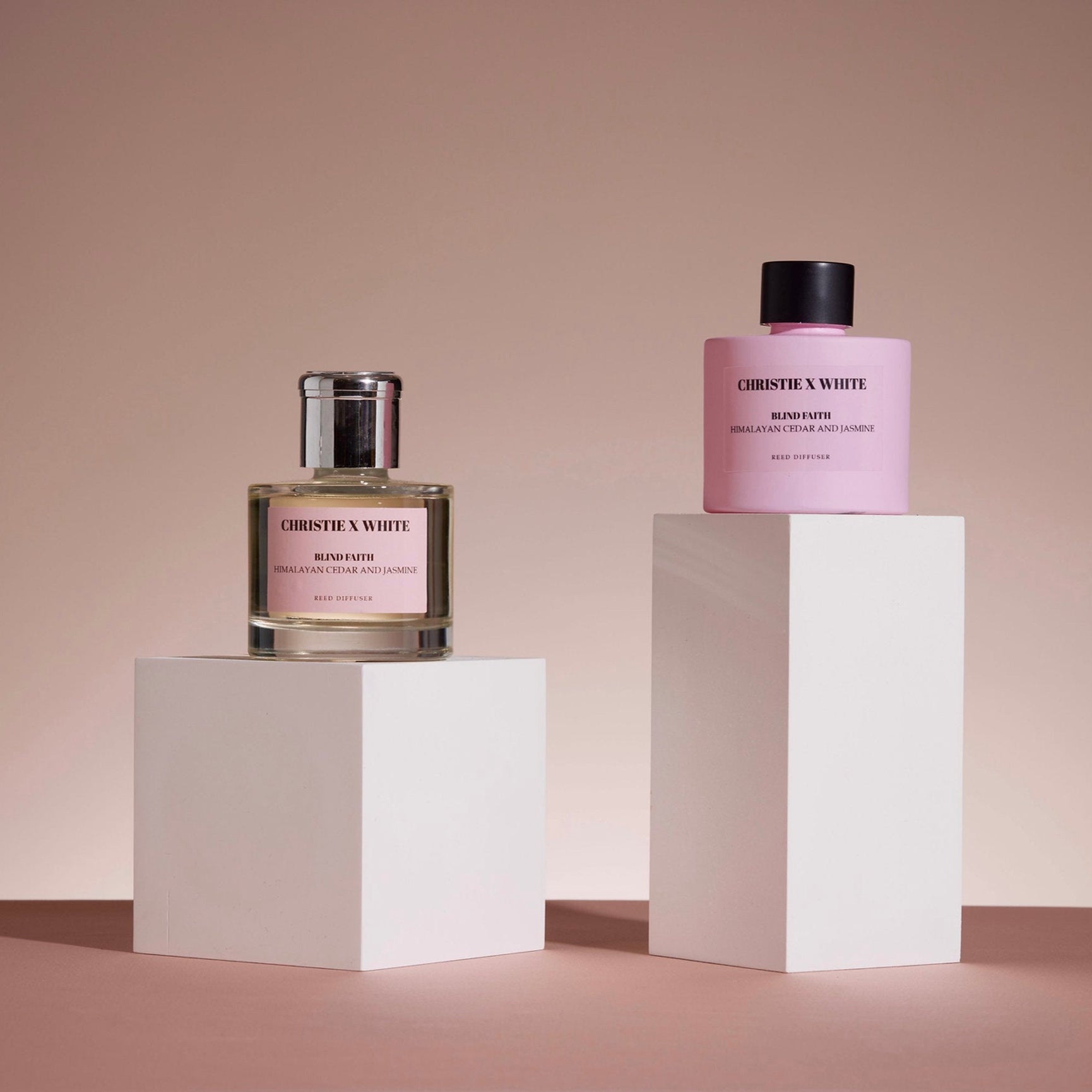 Two perfume bottles on white pedestals against a beige background