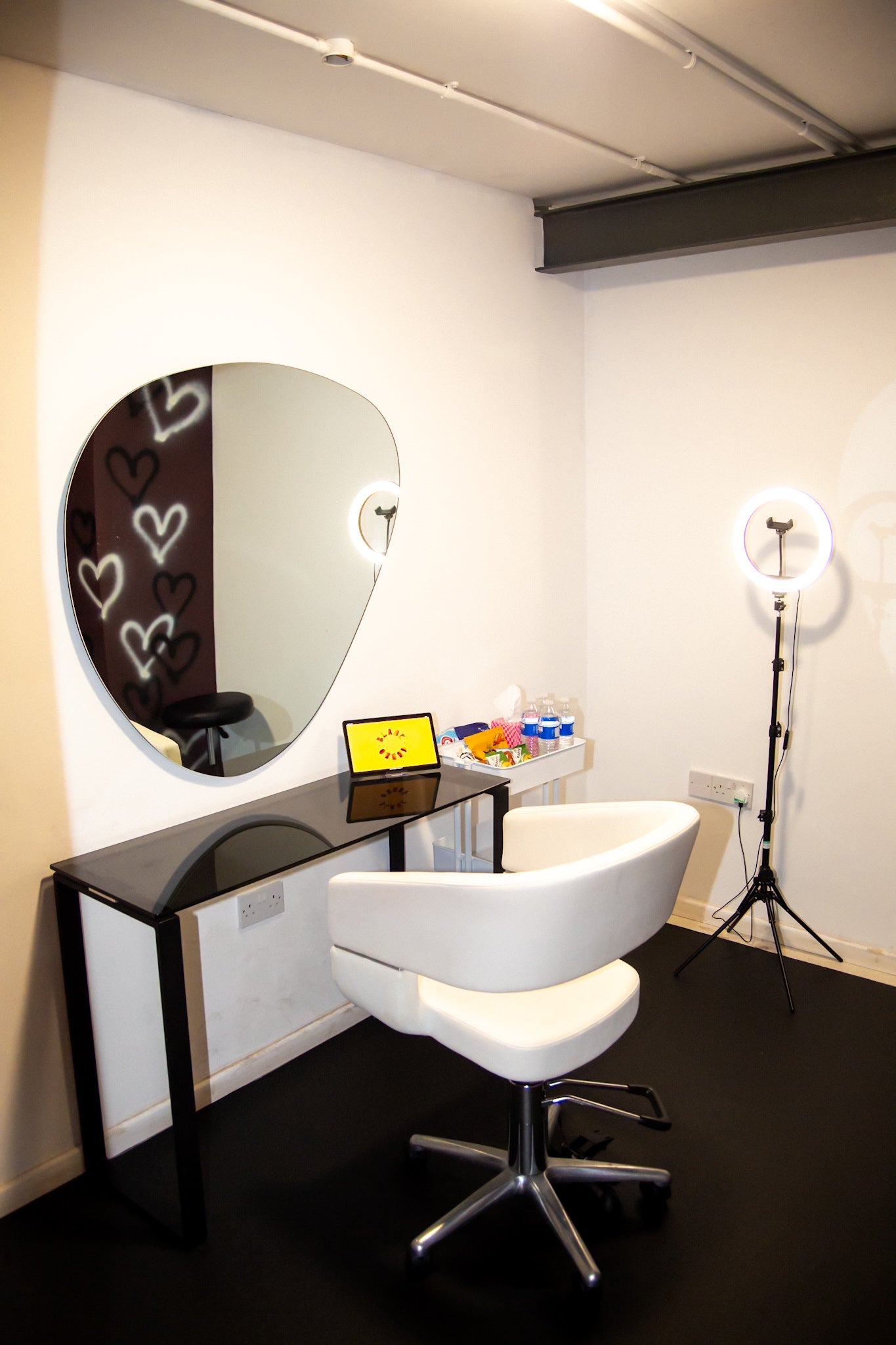 Studios beauty pod room with black flooring, ring light, snack bar, and heart drawn graffiti