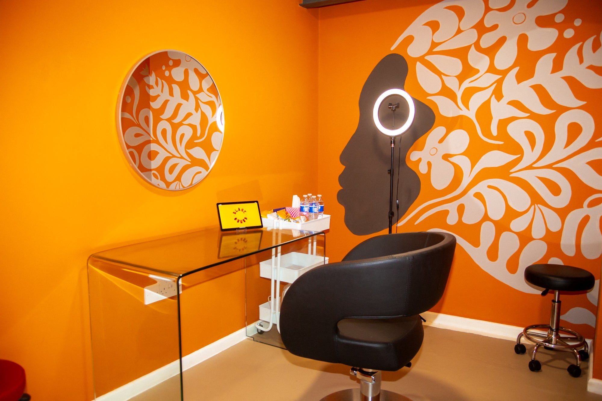 Modern studio setup with clear desk, black chair, and decorative wall art in an orange room.