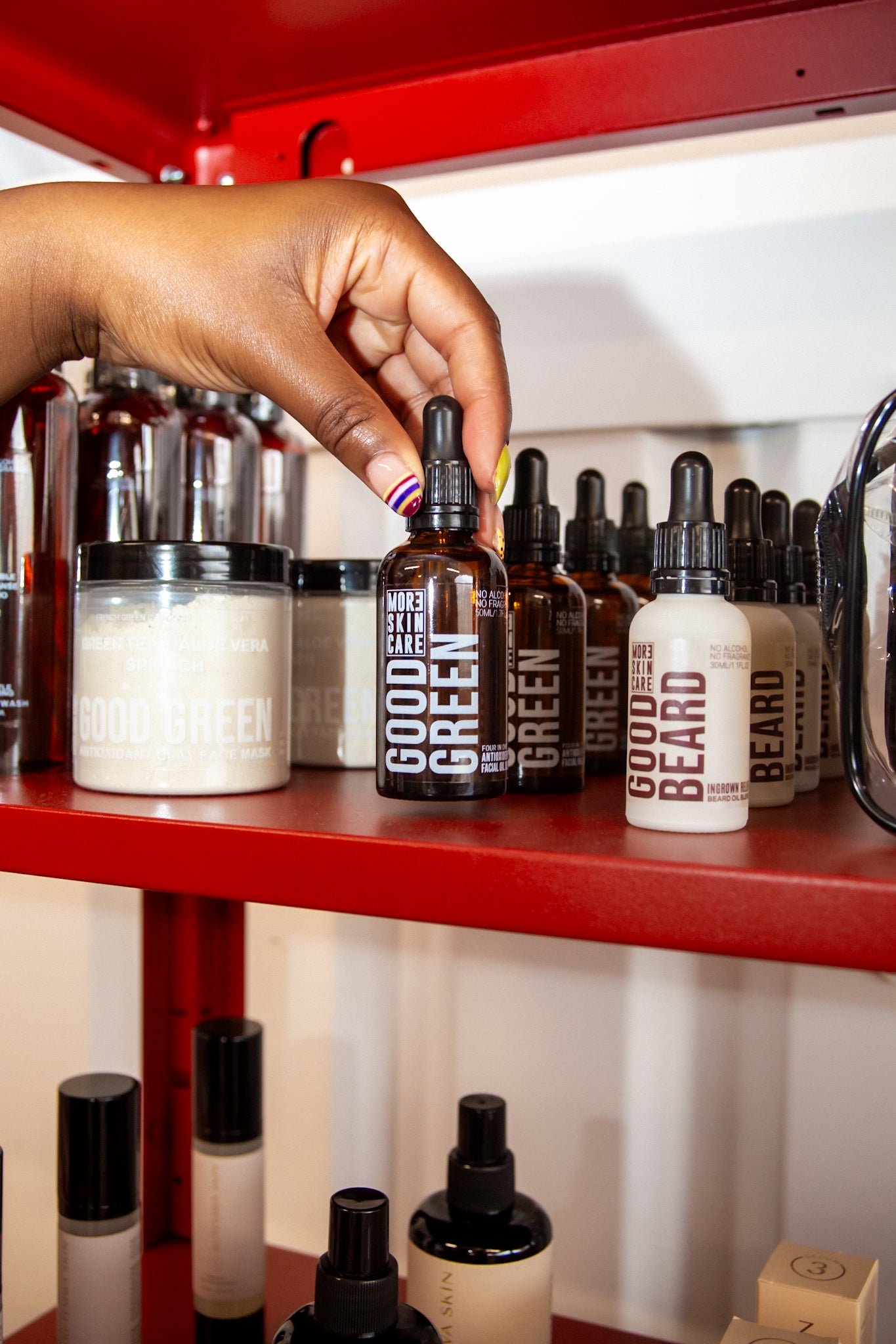 Hand selecting a bottle from a shelf of skincare and hair care products by MOR3SKIN