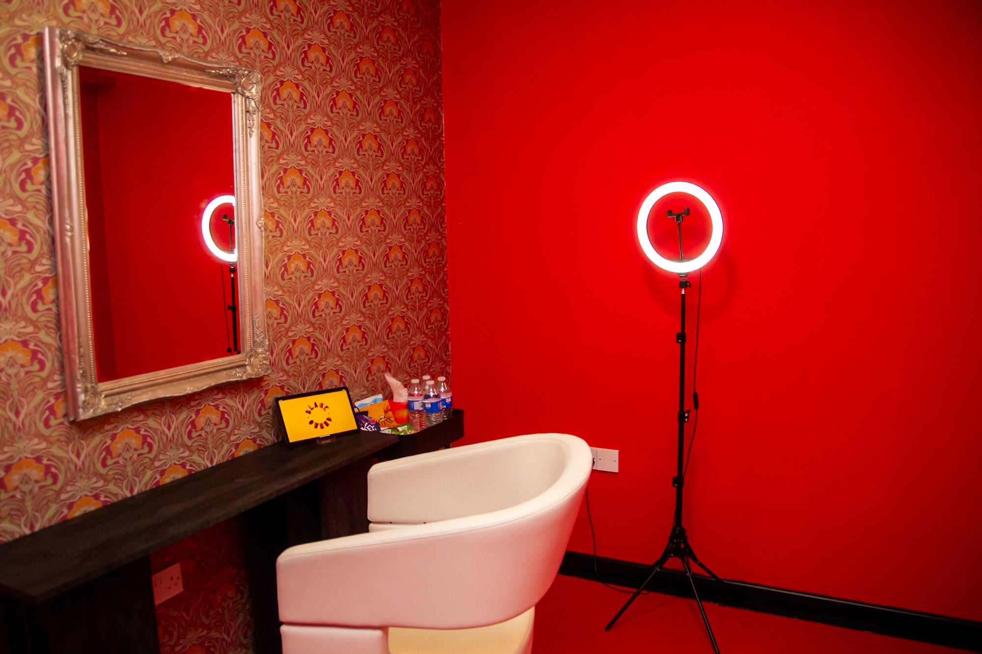 Studio pod room with red walls, a mirror, ring light and a comfy chair.